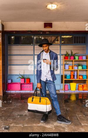Smiling young man with bag using smartphone Stock Photo