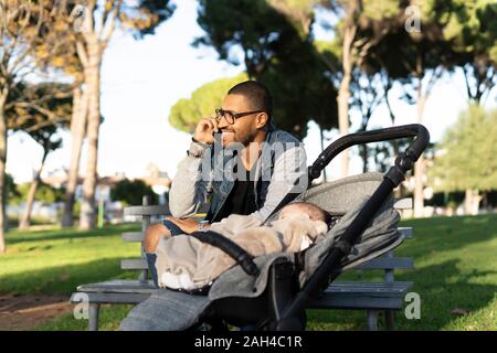 Working father in a park,  talking on the phone, with baby in pram Stock Photo