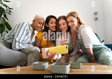 Four women sitting on couch taking a selfie Stock Photo