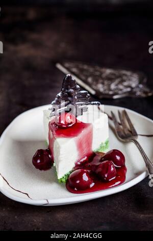 Piece of no-bake cheesecake, decorated with chocolate Christmas trees on plate with hot cherry sauce Stock Photo