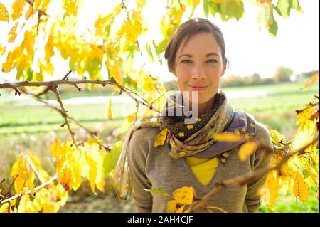 Portrait of woman at twigs with autumn leaves looking at camera Stock Photo
