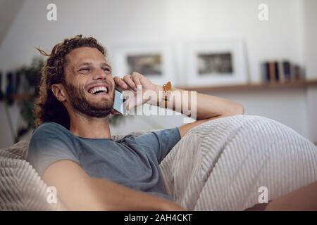 Laughing young man relaxing in beanbag at home talking on the phone Stock Photo