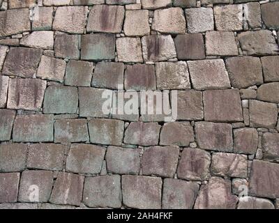 Natural rock blockwork in a wall with green and lilac colours caused by algae and lichen growth - suitable for a graphical background. Stock Photo