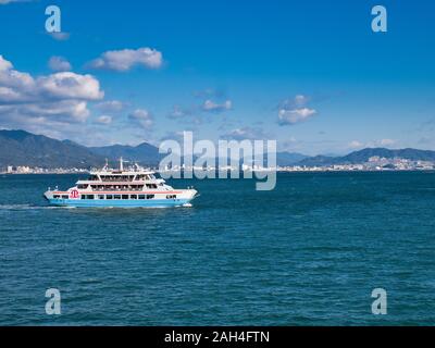 A roll-on / roll-off car ferry loaded with passengers travels between Miyajimaguchi Station and Miyajima Island in Hiroshima Bay. Stock Photo