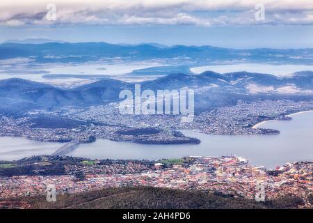 Elevated aerial view over HObart city on shores of Derwent river and harbour from hights of Mt Wellington on a cloudy winter day. Stock Photo