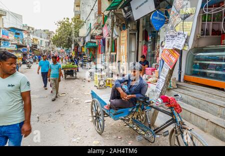 Local man resting on a tricycle: Street scene in Mahipalpur district, a suburb near Delhi Airport in New Delhi, capital city of India Stock Photo