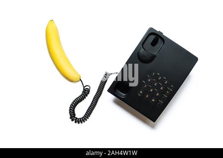 Creative photo of a simple modern black push-button telephone with a bright yellow banana instead of a handset isolated on a white background. Stock Photo