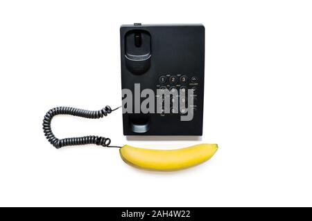 Creative photo of a simple modern black push-button telephone with a bright yellow banana instead of a handset isolated on a white background. Stock Photo