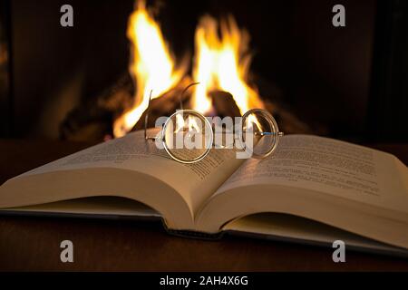 close up of vintage eyeglasses on open book with fireplace background Stock Photo