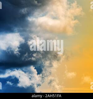 Amazing view of dramatic blue thunderclouds and stunning yellow-golden fluffy clouds illuminated by rays of sun. Natural meteorology background, cloud Stock Photo