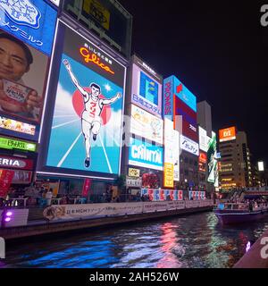 OSAKA, JAPAN - OCTOBER 14, 2019:  The bright and flashy billboards along the Dotonbori canal with the symbol of the city, the Glico Running Man at nig Stock Photo