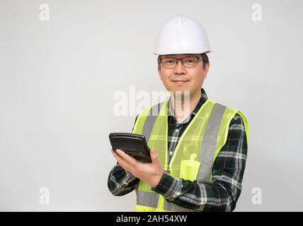 A middle-aged Asian man wearing a white work cap and work suit holding a calculator in his hand. Stock Photo