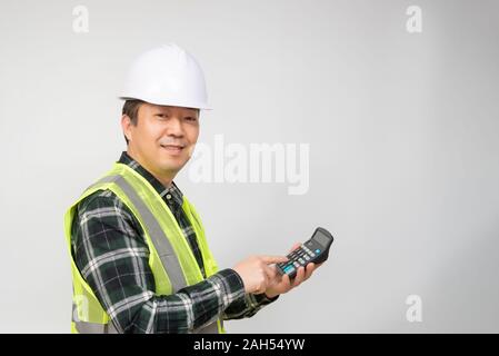 A middle-aged Asian man wearing a white work cap and work suit holding a calculator in his hand. Stock Photo