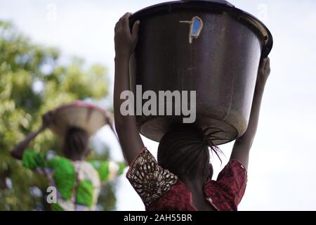 Backshot Of A Young African Girl Carrying Heavy Water Bucket Back Home From the Village Borehole Stock Photo