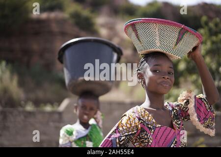 Two Proud African Girls Carrying Heavy Household Items On Their Head Stock Photo