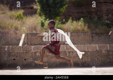 Colourfully Dressed Little African Girl Running With Her White Scarf Flowing In The Wind Stock Photo