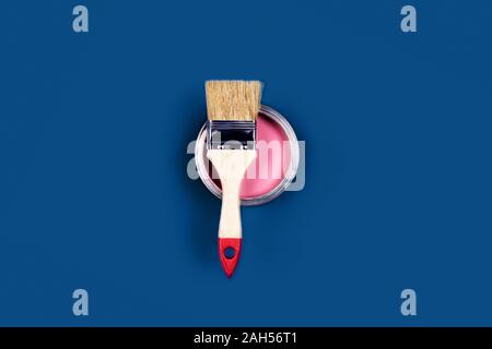 Renovation concept. Classic blue background with pink paint jar and one brush located on it. Flat lay, top view, copy space. Stock Photo