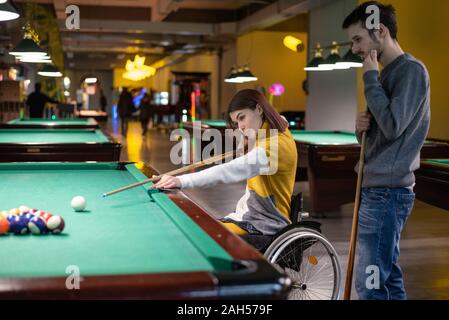 Beautiful disabled girl in a wheelchair playing billiards with her friend Stock Photo
