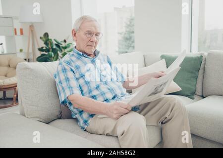 Portrait of his he single nice focused concentrated peaceful calm granddad, sitting on divan reading world news paper in light white interior living-r Stock Photo