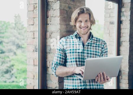 Portrait of charming man holding modern, technology smiling wearing checkered plaid shirt in industrial Stock Photo