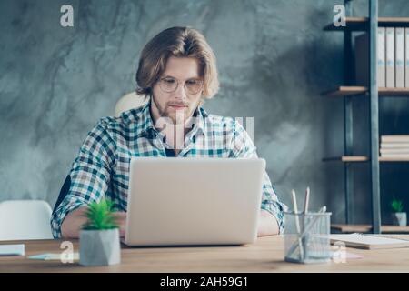 Portrait of focused person, using netbook wearing checkered plaid shirt eyeglasses eyewear sitting in industrial Stock Photo