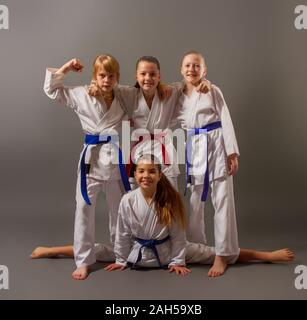 four little karate girls in white kimonos posing on a dark background in a good cheerful mood Stock Photo