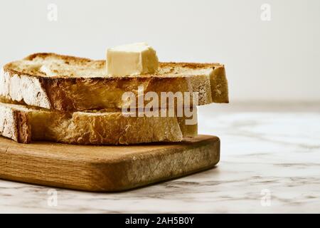 Slices of fried freshly baked bread with a piece of butter on top, lie on a wooden shelf on a marble table Stock Photo
