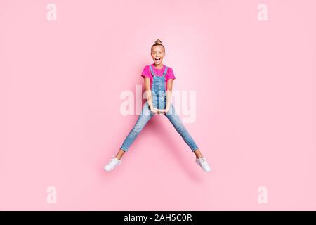 Full length body size photo of cute nice jumping girl doing splits wearing, fuchsia t-shirt screaming overjoyed isolated over pink color pastel backgr Stock Photo