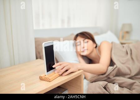 Annoying alarm. Woman lying in bed being woken by mobile phone, turning off noisy signal, closeup Stock Photo