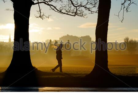 Edinburgh, Scotland, UK. 25th Dec 2019.  Cold, clear and bright with low ground mist on Christmas day at sunrise in Inverleith Park, with a view of Edinburgh Castle. Man walking in the park. Credit: Craig Brown/Alamy Live News Stock Photo