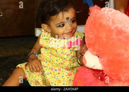 Little girl with teddy bear is looking at the camera. Female doctor on background. Stock Photo