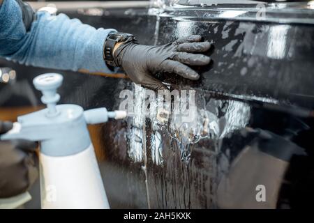 Car service worker splashing water on the car body, wetting it during anti-gravel film apply at the vehicle detailing service Stock Photo