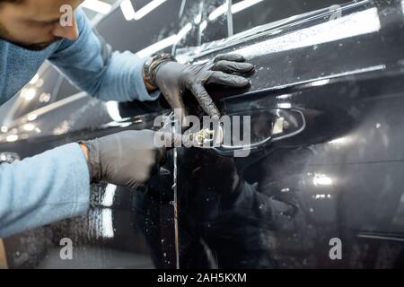 Worker sticking protective transparent film on a car body in place of the door handle, close-up view Stock Photo