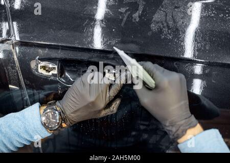 Worker sticking protective transparent film on a car body in place of the door handle, close-up view Stock Photo