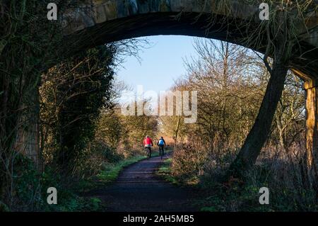 East Lothian, Scotland, United Kingdom, 25th December 2019. Christmas day exercise on the Haddington to Longniddry railway path with a couple riding bicycles seen through the arch of a bridge Stock Photo