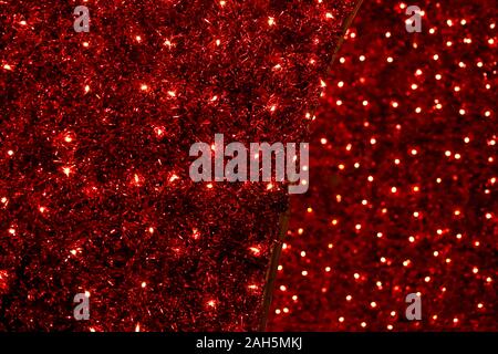 Red Christmas festive decorative background with tinsel, flashing lights and garlands. New Year lighting decoration in red and yellow color. Stock Photo