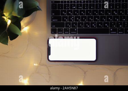 Kyiv, Ukraine. Modern MacBook Laptop with retina computer and red Iphone 11 on white in interior with domestic plants, lights, bokeh. Technologies, on Stock Photo