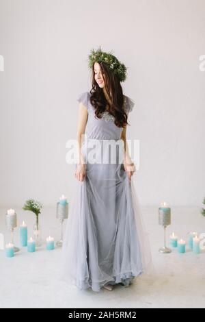 Beautiful young girl in a gray evening dress and a wreath of pine and eucalyptus on her head poses on the background of wedding scenery. Bridesmade po Stock Photo