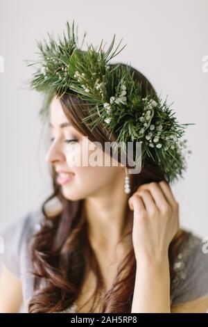 Beautiful young girl in a gray evening dress and a wreath of pine and eucalyptus on her head poses on the background of wedding scenery. Bridesmade po Stock Photo