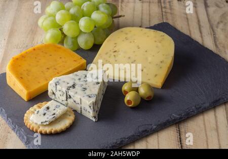 Cheese board with three cheeses, gouda with pimento, gouda with cumin seeds and roquefort blue cheese close up on rustic wooden background Stock Photo