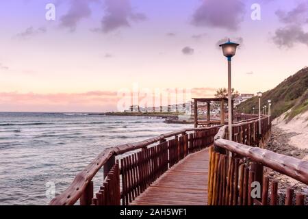 Boardwalk leads past beach and sea in Gonubie iin East London, South Africa in the evening sunset Stock Photo