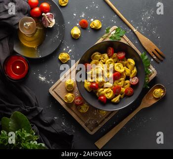 Ravioli with tomatoes on black plate in rustic homemade food environment, dark food Stock Photo