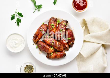 Bacon wrapped grilled chicken wings on plate over white stone background. Tasty snack from chicken meat, bacon in sweet, sour, salty and spicy sauce. Stock Photo
