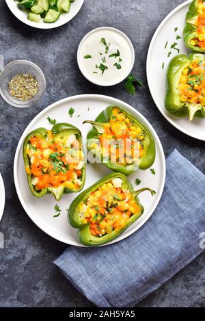 Healthy diet or vegetarian food concept. Baked green bell peppers filled with corn, carrot, cauliflower on white plate over blue stone background. Top Stock Photo