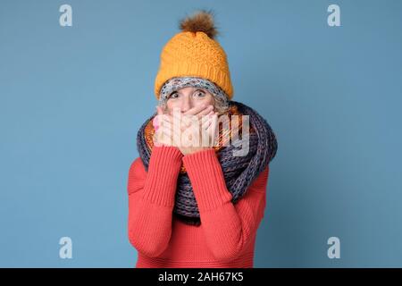 Woman in winter clothes having astonished expression, covering mouth with hands Stock Photo