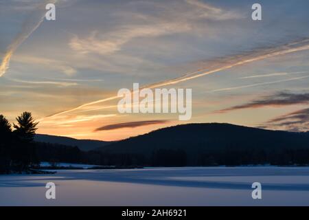 Cold Sunrise Over Tree Covered Hills And Frozen Water With Snow At Red House Lake, Allegany State Park, New York Stock Photo