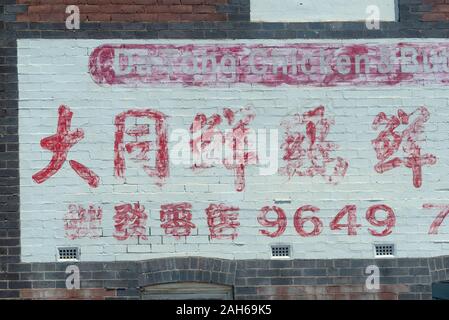 A hand painted sign with red lettering on a white background with Chinese and western lettering and numbers, some partly rubbed out and painted over Stock Photo