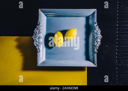 Minimalism and lemons on squared blue tray on yellow and black background. Top view with space for text. Stock Photo