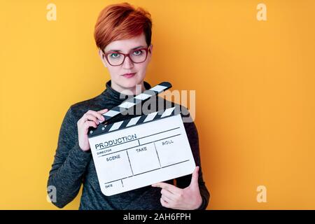 redhead woman holding movie clapper against yellow background cinema concept Stock Photo
