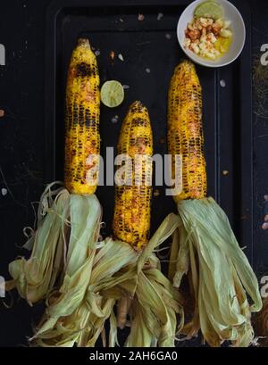 Grilled corn on cob with cheese, paprika, sea salt and lime, indian street food, Roasted corn on a black plate, ideas for barbecue and grill parties Stock Photo